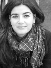 Das Foto ist ein Schwarz-Weiß Portrait von Susanna Isern. Sie hat lange, glatte, dunkle Haare und trägt einen karierten Schal.
