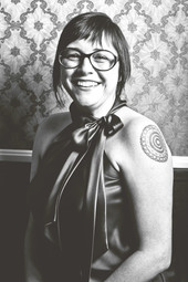 Porträt der Autorin Missy Marston in Schwarz-weiß - grinsend vor einer Mustertapete.